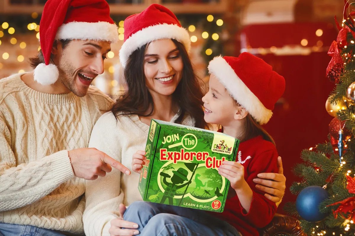 Mum, dad and daughter in Christmas hats opening the Explorer Club box by the tree