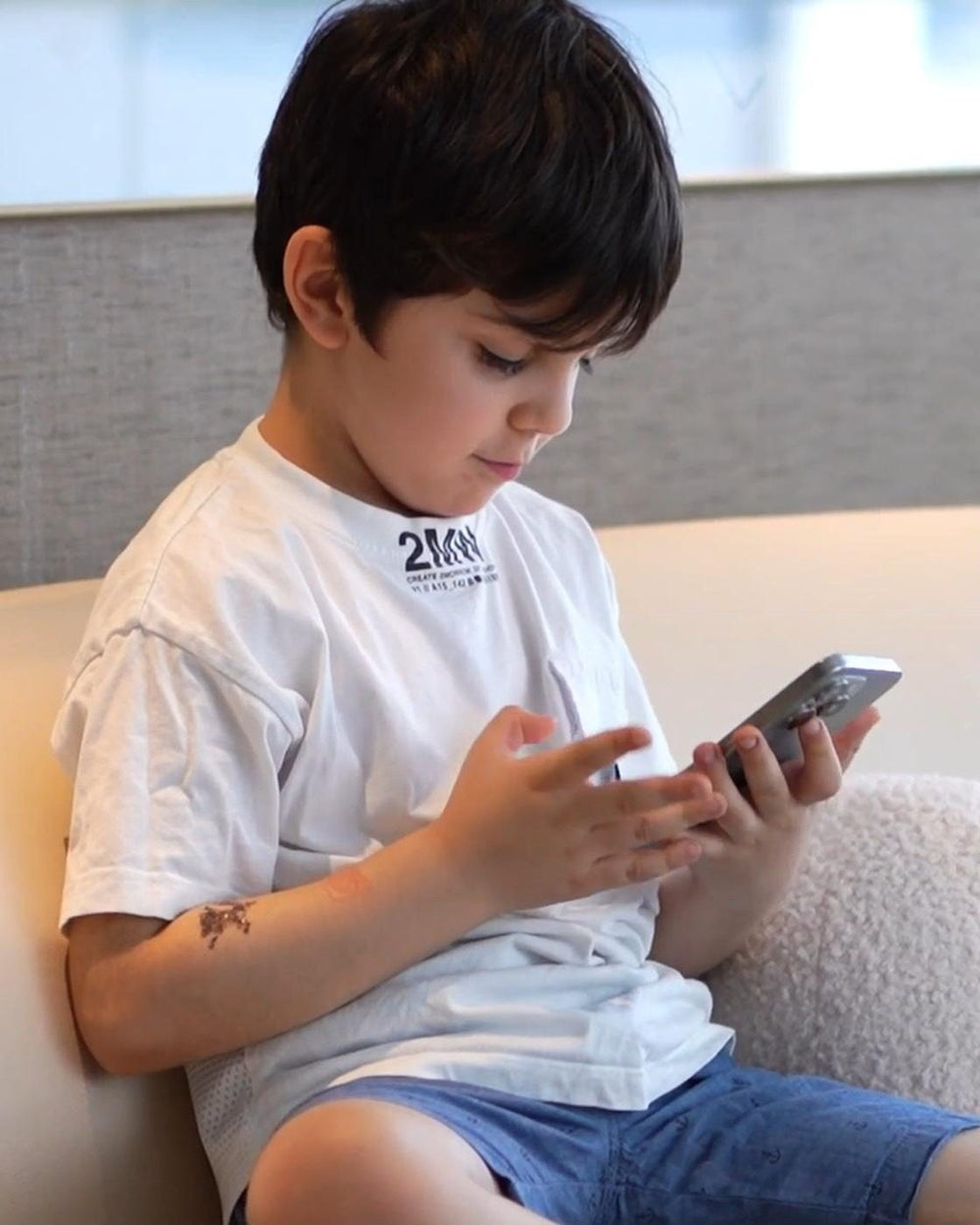 Boy on a sofa, head down, staring at a phone