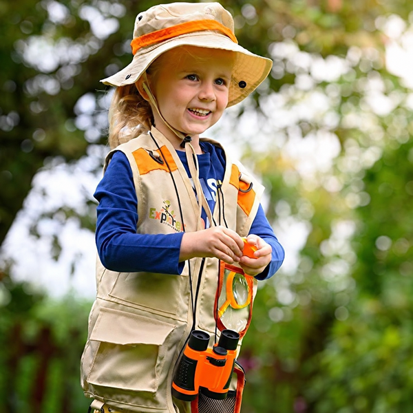 Child exploring outdoors in an orange explorer vest and hat