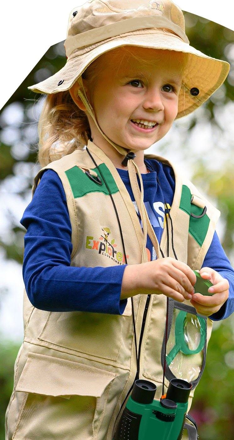 Girl in the explorer hat and vest outside, smiling, with the binoculars round her neck
