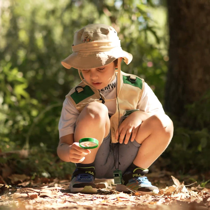 Boy in the explorer kit crouching with his magnifying glass