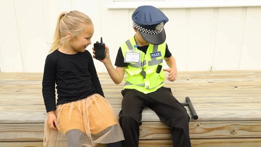 Two children on a garden bench, one in the police set talking into the walkie-talkie